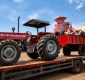 Red Massey Ferguson 385 4WD tractor on a flatbed trailer with a red scrap wagon and piled debris against a blue sky