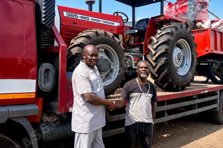 Two men shake hands beside a red Massey Ferguson 385 4WD tractor loaded on a flatbed truck outdoors on a sunny day with clear blue sky in the background