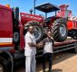 Two men shake hands beside a red Massey Ferguson 385 4WD tractor loaded on a flatbed truck outdoors on a sunny day with clear blue sky in the background